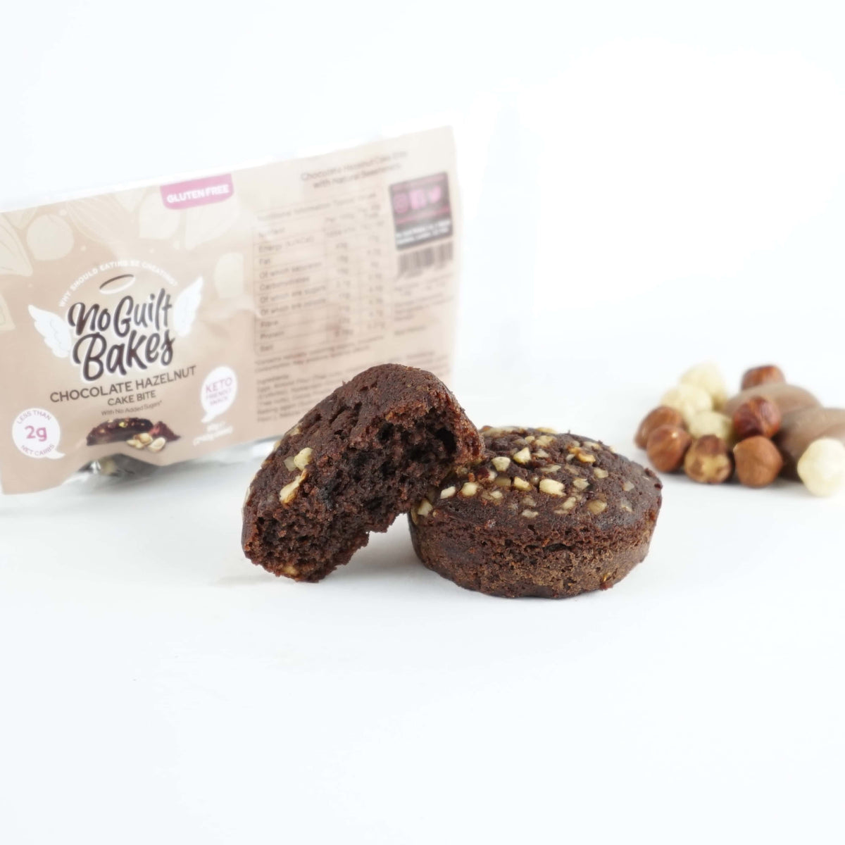 A Chocolate Hazelnut muffin with nuts and a No Guilt Bakes Gift for purchase over £30 bag next to it.