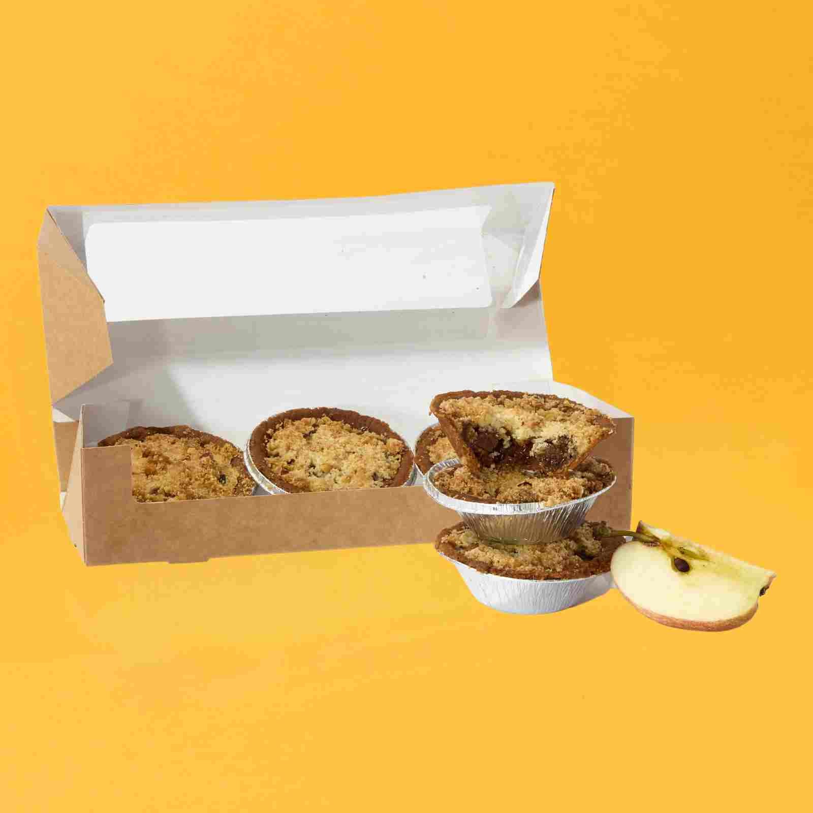Two No Guilt Bakes Apple Crumble Tarts in a box on a yellow background.