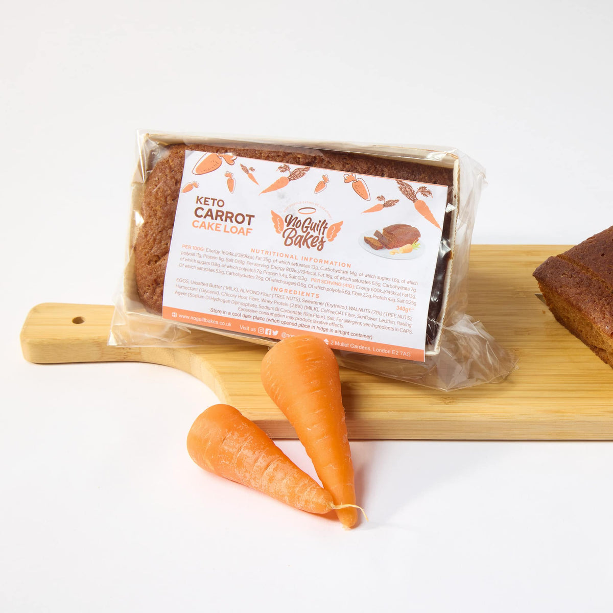 A package of low-carb, keto-friendly Carrot Keto Cake Loaf and fresh carrots on a cutting board by No Guilt Bakes.
