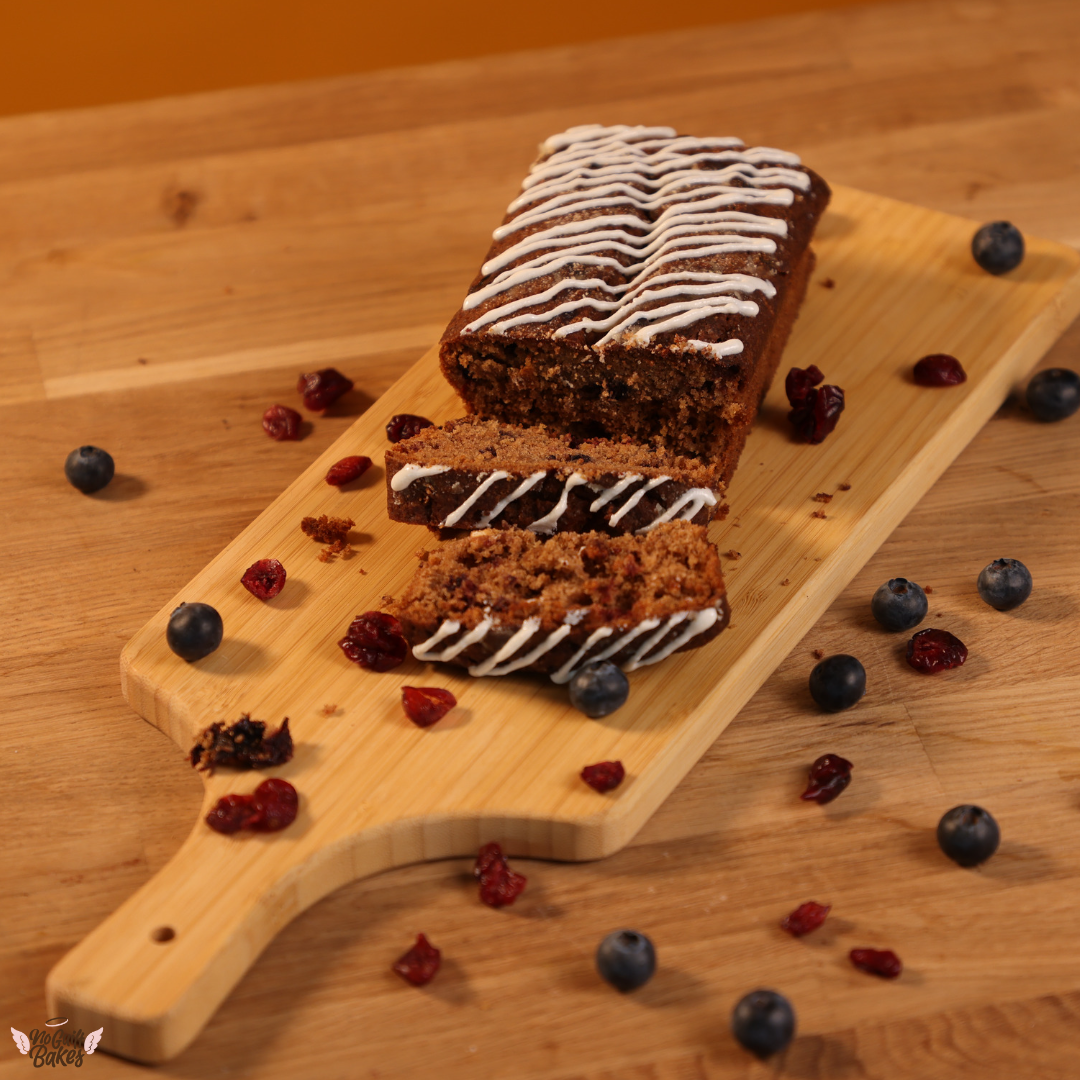 A slice of Low Carb Fruit Loaf Cake - Gluten Free with blueberries and cranberries on a wooden board from No Guilt Bakes.